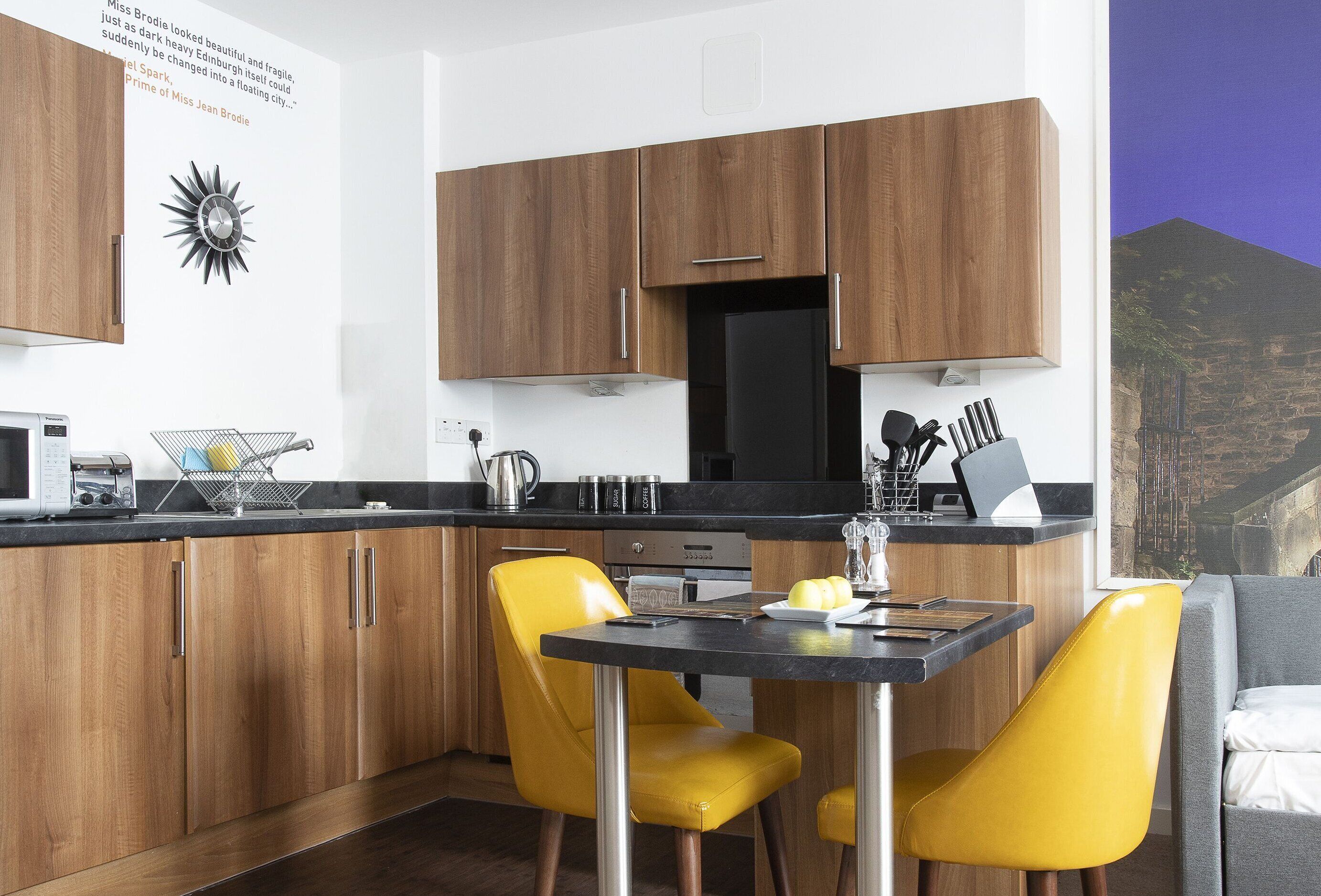 A modern kitchen with wooden cabinets, a black refrigerator, and a yellow chair.