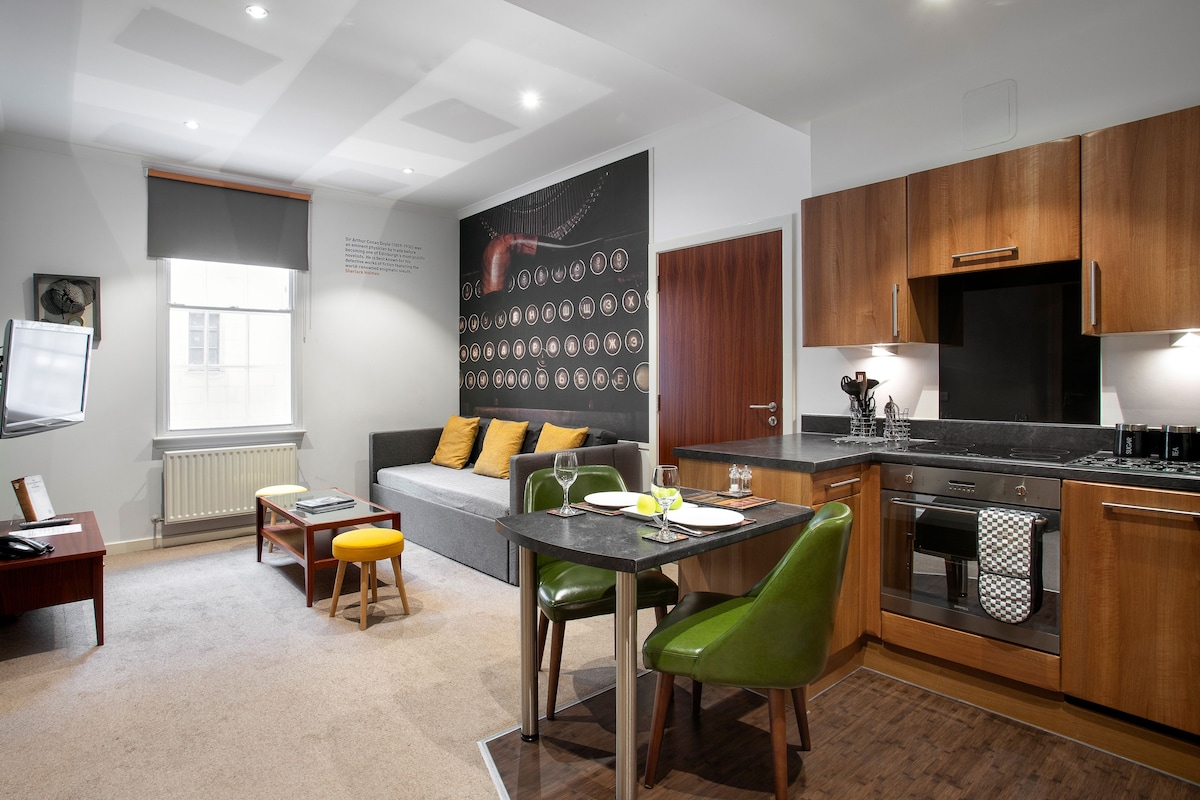 A modern kitchen with wooden cabinets, a dining table with chairs, a sofa, and a large abstract wall art piece.