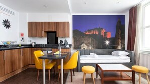 A modern hotel room with a dining area, a bed with a view of a castle, and wooden cabinets. - Stewart by Heeton Concept (Edinburgh)