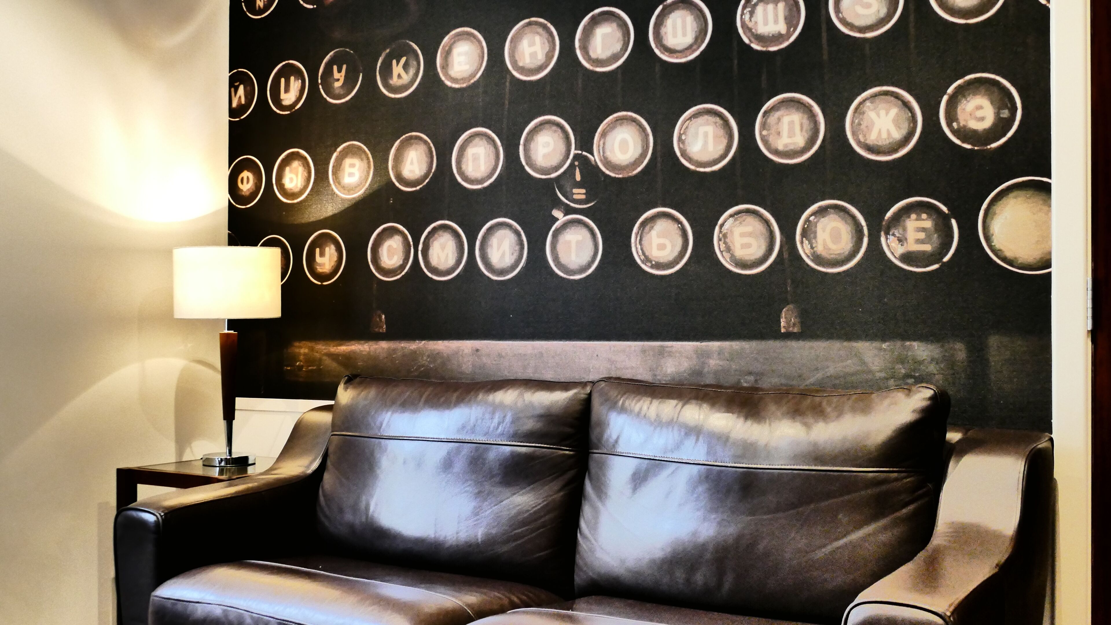 A leather sofa with a high backrest and armrests, positioned against a wall with circular decorative elements.
