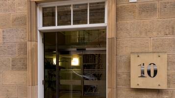 The exterior of the Stewart APT Hotel in Edinburgh, Scotland, featuring a large glass entrance, a signboard above the entrance, and a number plate indicating the address.