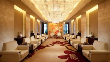 Un hall d’hôtel luxueux, doté d’un espace salon central, d’élégants lustres et d’une fresque florale sur le mur.