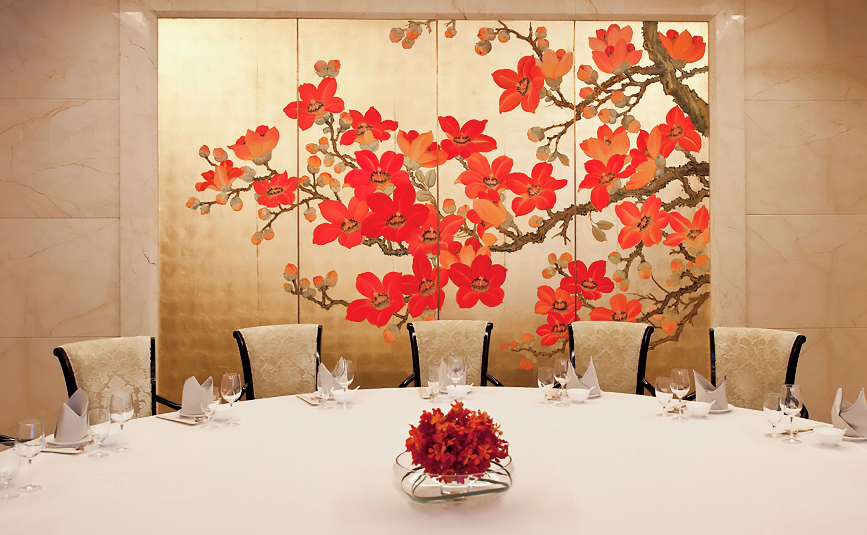 A conference table with six chairs, a vase with red flowers, and a decorative wall panel with red flowers.