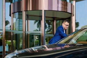 A man in a blue suit exiting a modern building with a glass entrance, which appears to be a hotel. - Hilton Guangzhou Baiyun-Canton Fair Free Shuttle Bus Service and Free Registration (Guangzhou)