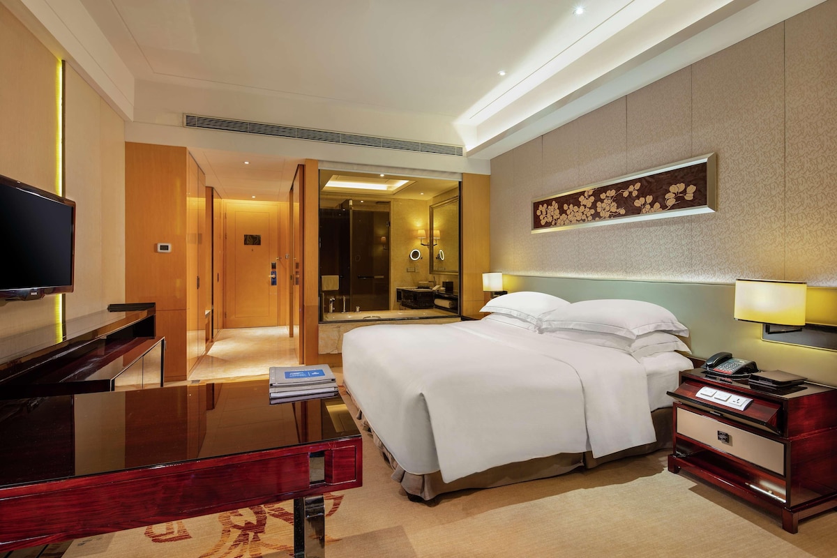 A hotel room with a bed, bedside table, lamp, and a TV.