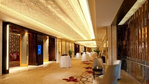 Un pasillo amplio en un hotel, con una alfombra larga y elegante, una fila de mesas redondas y un diseño de techo moderno.