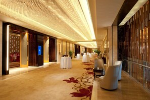 Un pasillo amplio en un hotel, con una alfombra larga y elegante, una fila de mesas redondas y un diseño de techo moderno.