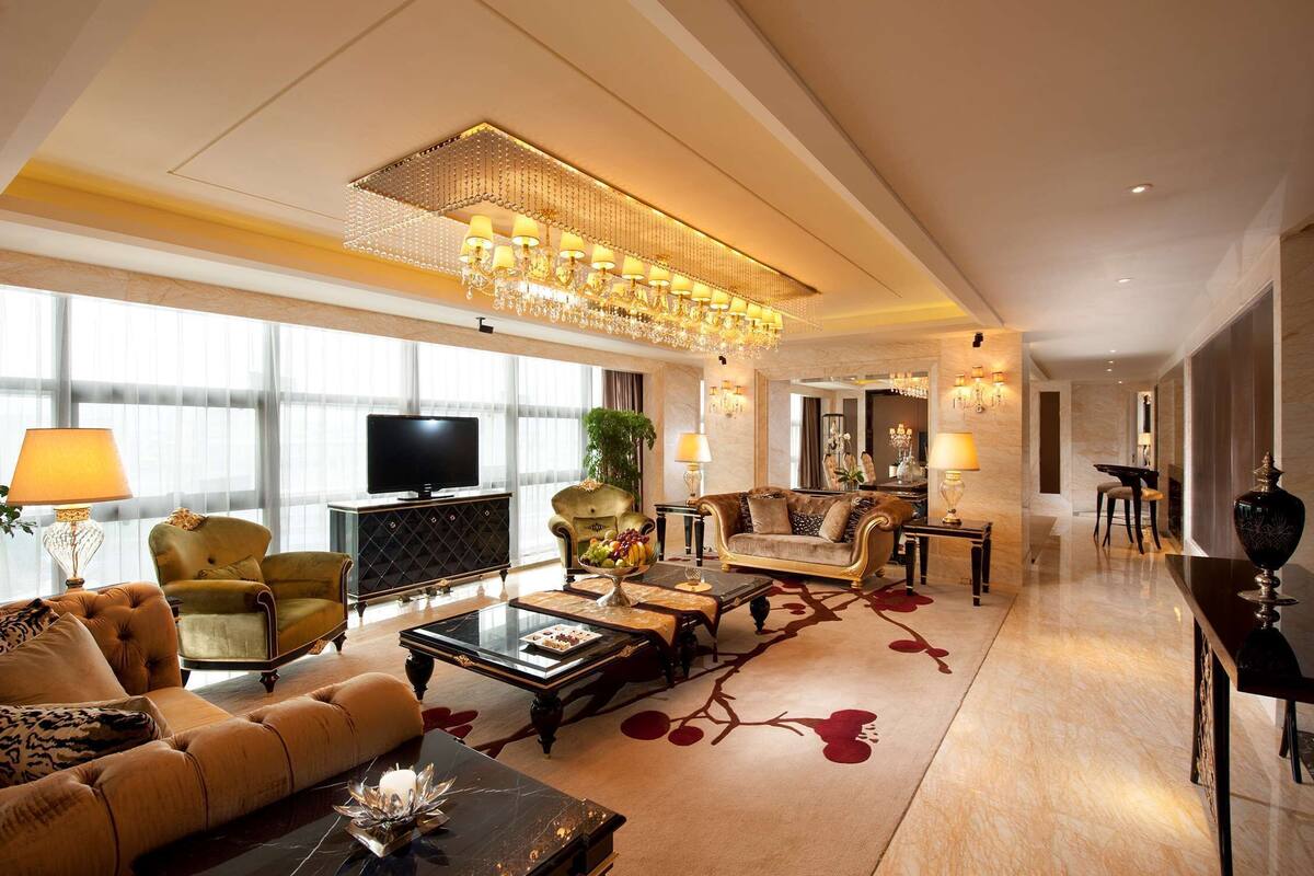 A spacious living room with a large chandelier, comfortable seating, a television, and a large window providing natural light.