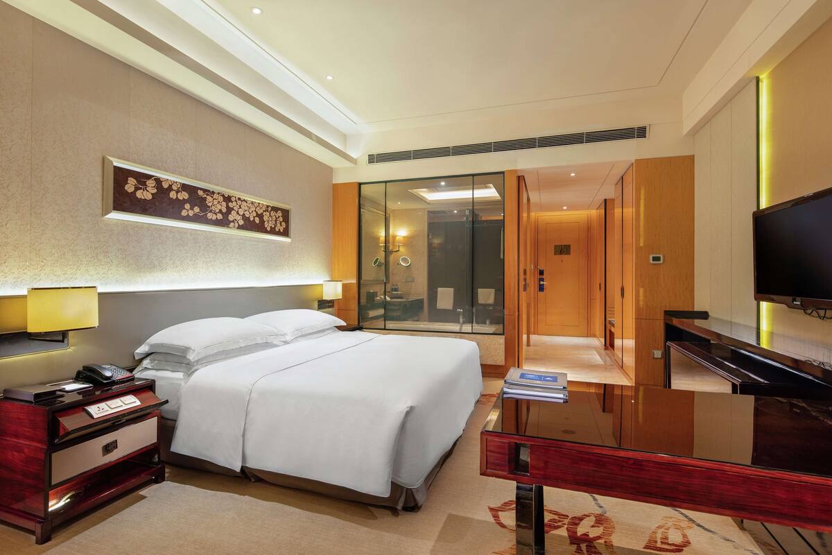 A hotel room with a bed, bedside table, lamp, and a television.