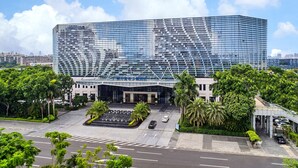 Un hotel moderno con fachada de vidrio, un vestíbulo amplio y un estacionamiento con automóviles.