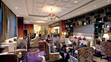 A hotel lobby with a chandelier, seating area, and a decorative bookshelf.