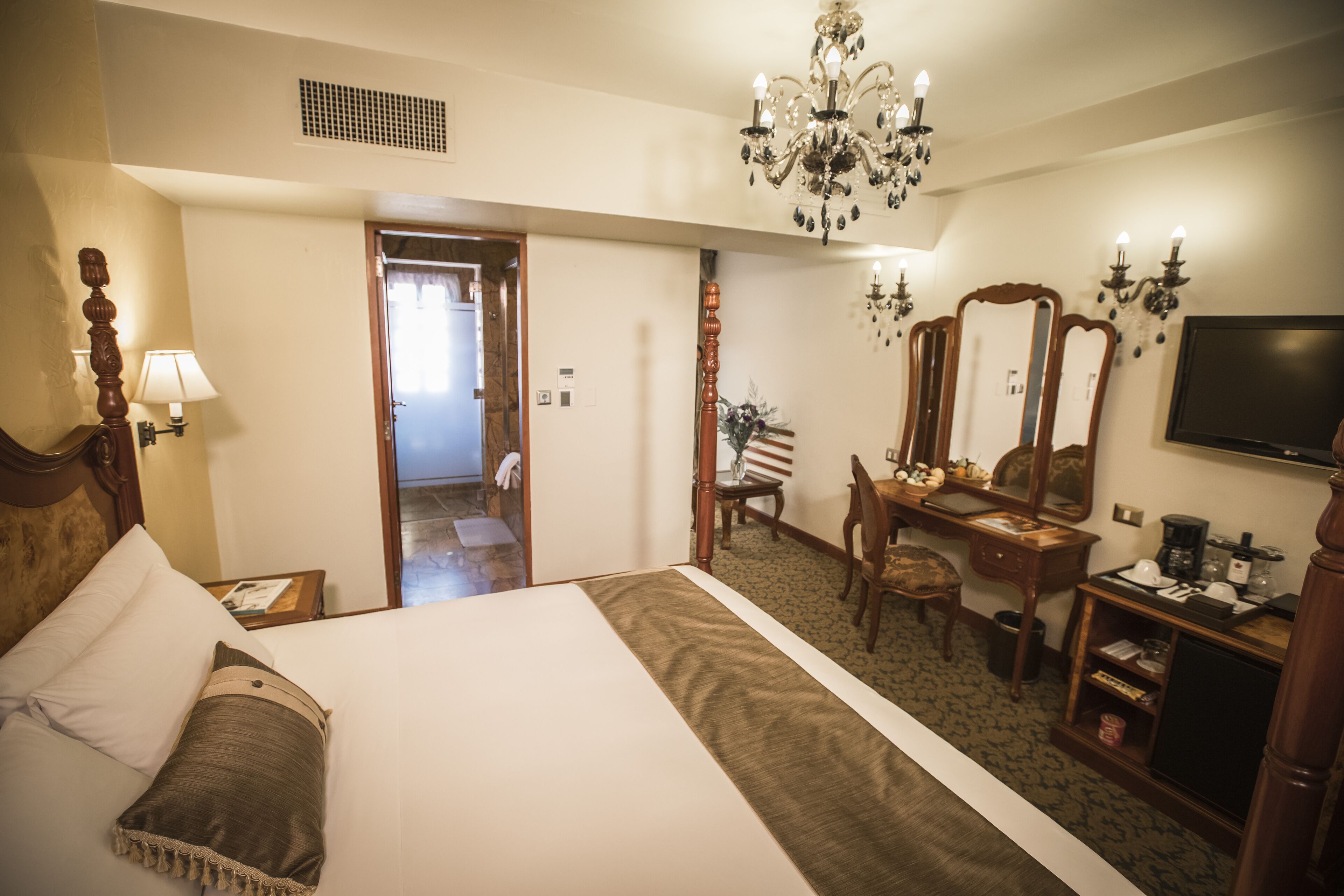 Habitación de hotel con una cama grande, un escritorio, una silla, un televisor y una araña.