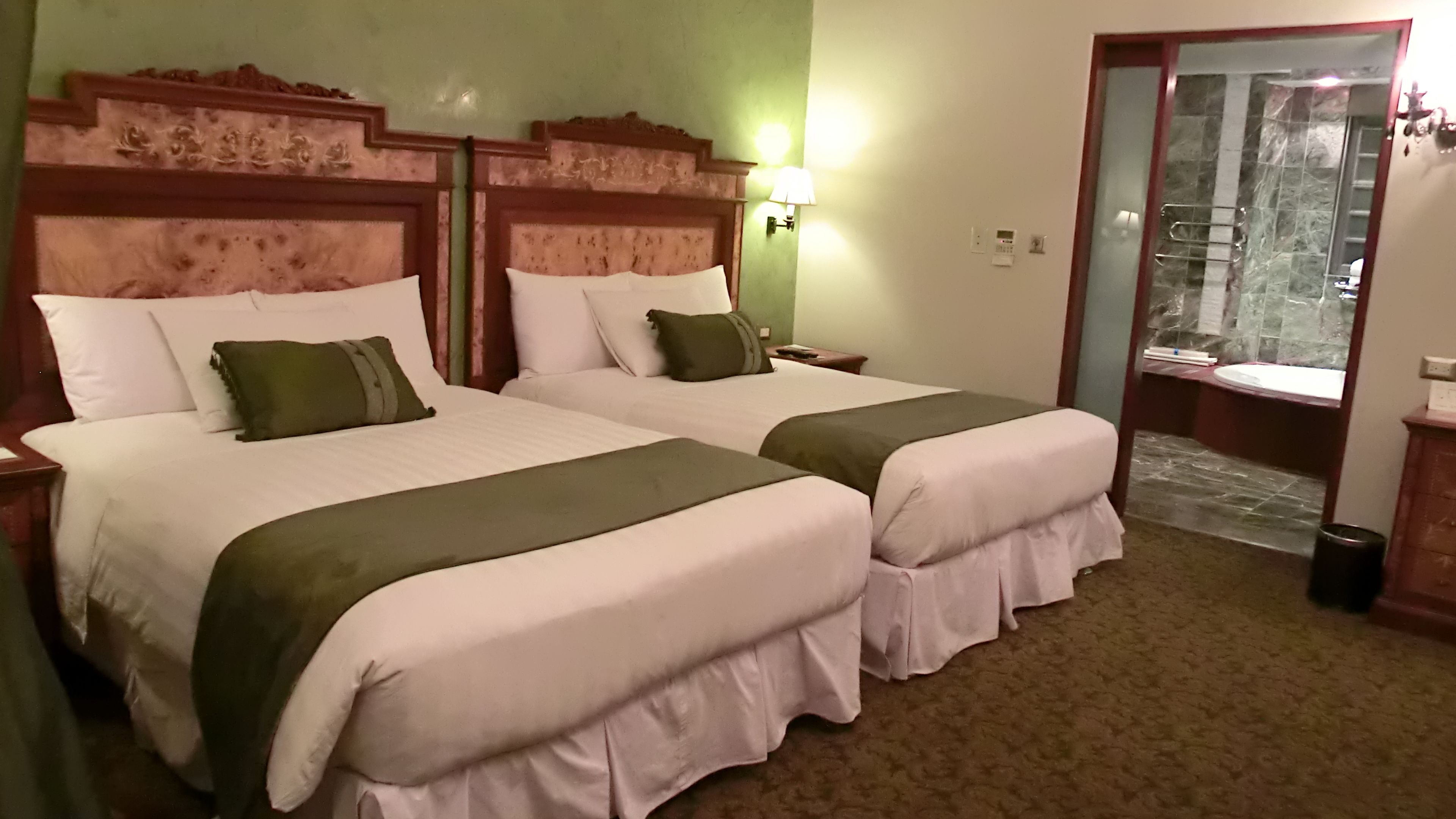 Habitación de hotel con dos camas, cada una con cabecero, mesita de noche y lámpara.