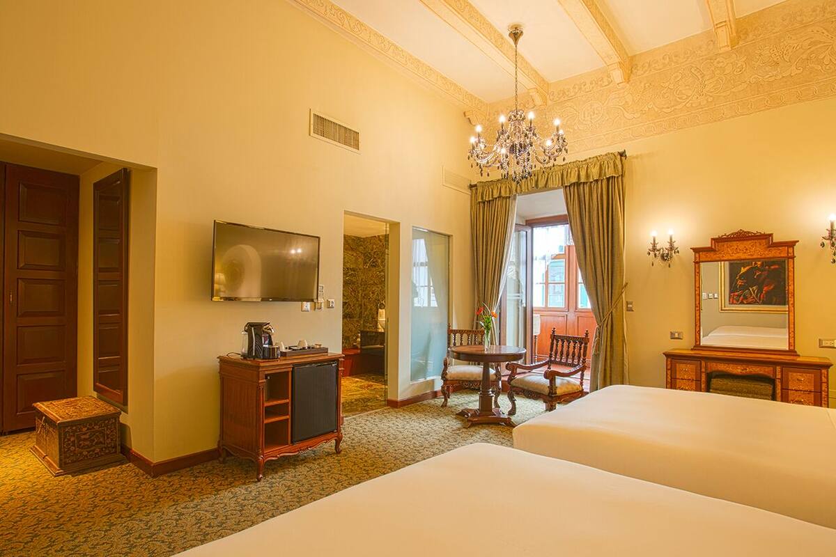 Een hotelkamer met twee bedden, een televisie, een houten kast, een kroonluchter en een schilderij aan de muur.
