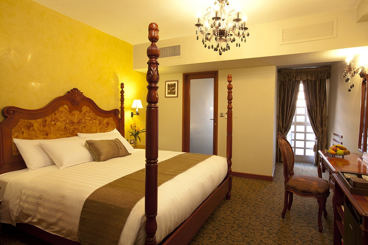 Una cama con dosel con cabecera de madera, un candelabro y una mesa de comedor con fruta.