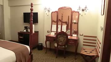 Habitación de hotel con una cama, un escritorio de madera con un espejo, una silla, una mesita con teléfono y un televisor en la pared.