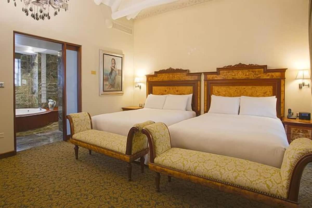 Hotelkamer met twee bedden, een kroonluchter, een schilderij en een badkamer zichtbaar door een geopende deur.