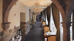 A corridor with stone arches, a chandelier, and tables with breakfast items.