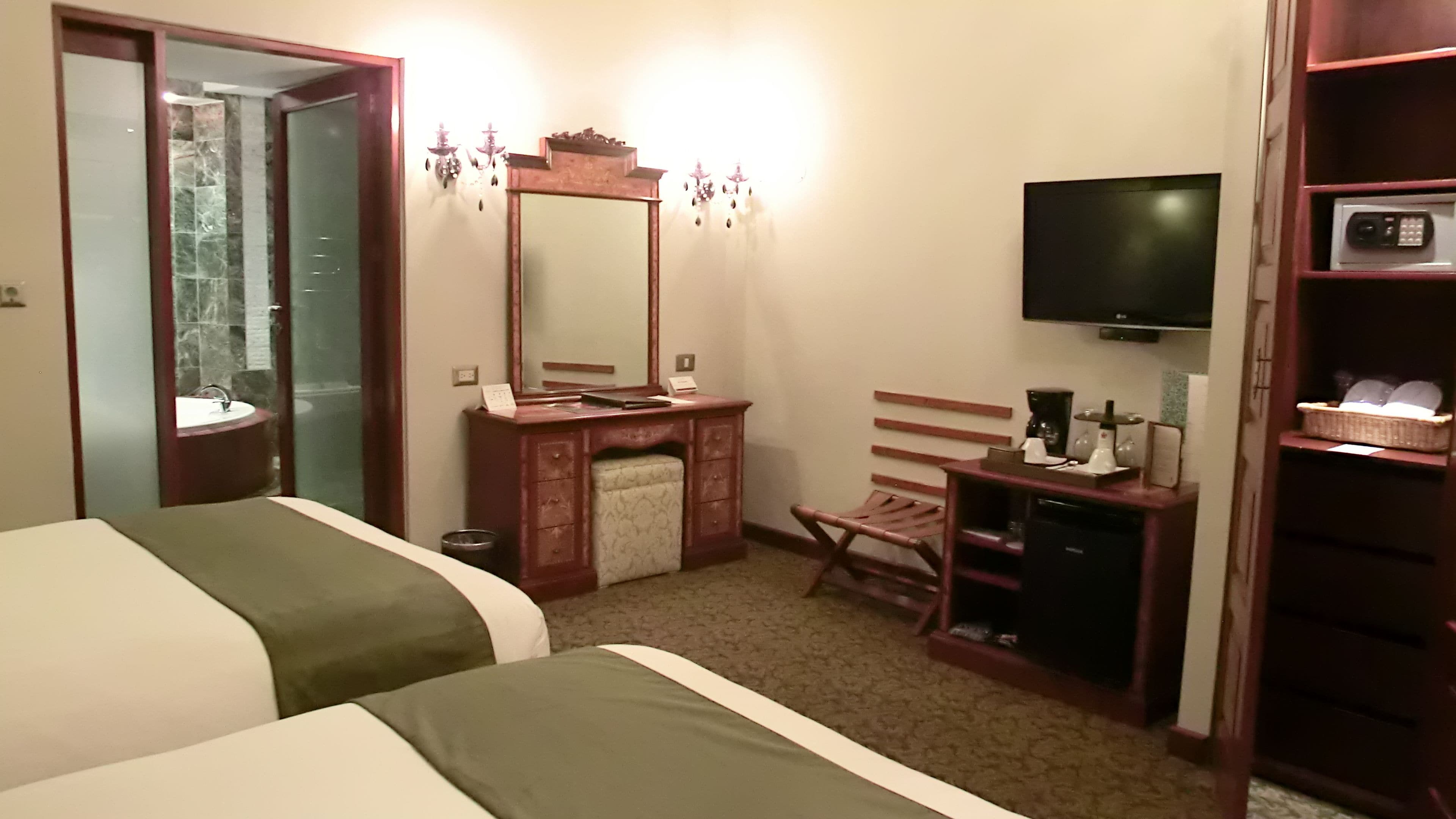 A hotel room with two beds, a wooden desk with a mirror, a television, and a small seating area.