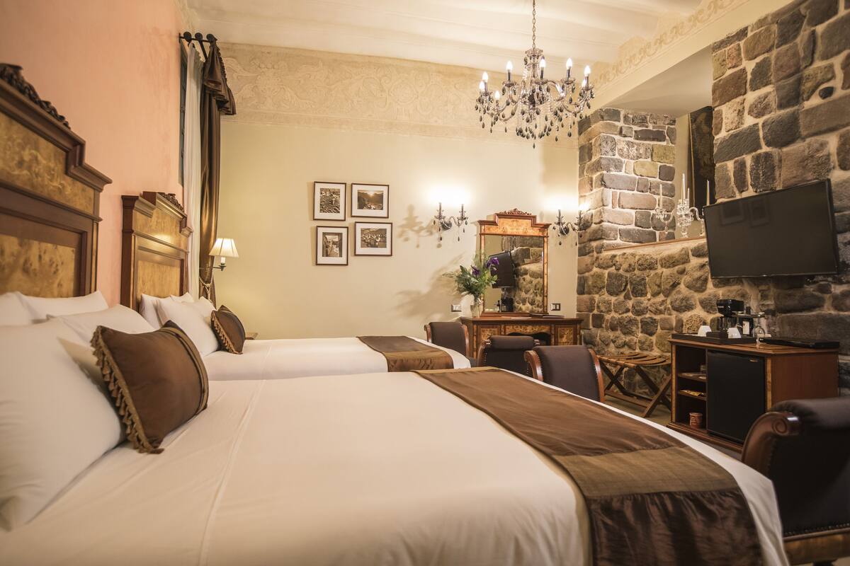 Een hotelkamer met twee bedden, een stenen muur, een televisie en een kroonluchter.