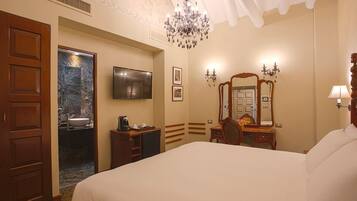 Una habitación de hotel con una cama grande, televisión, candelabro, espejo y armario de madera.