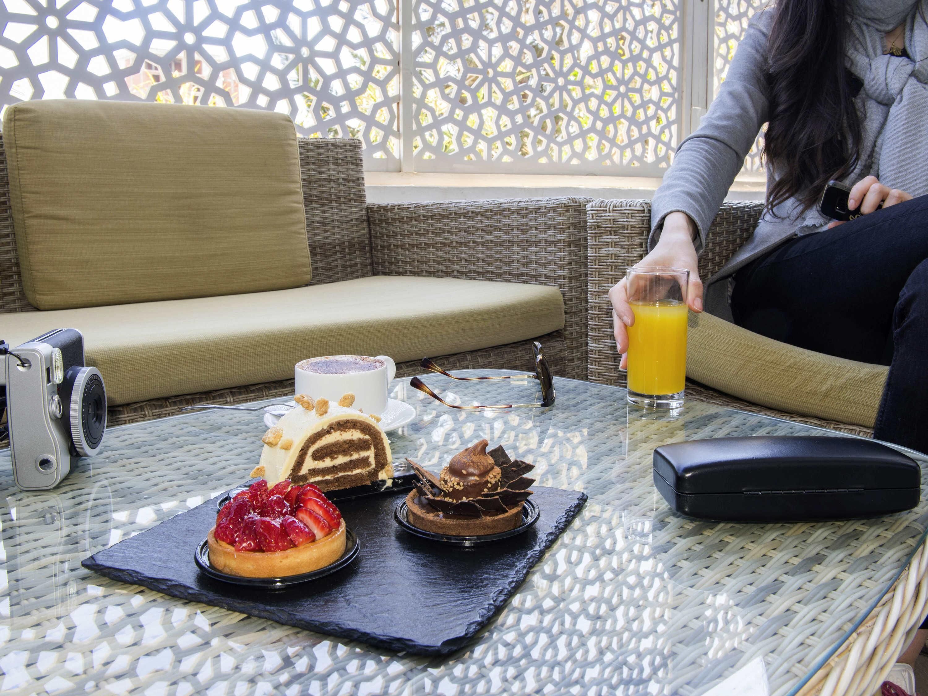 Ein Glastisch mit Kuchen, einer Kaffeetasse und einem Glas Orangensaft.
