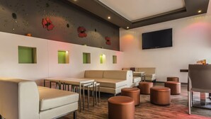 Ein stilvoller Lounge-Bereich mit Sofas, Tischen und Hocker, einem Flachbildfernseher sowie dekorativen Wandbildern.