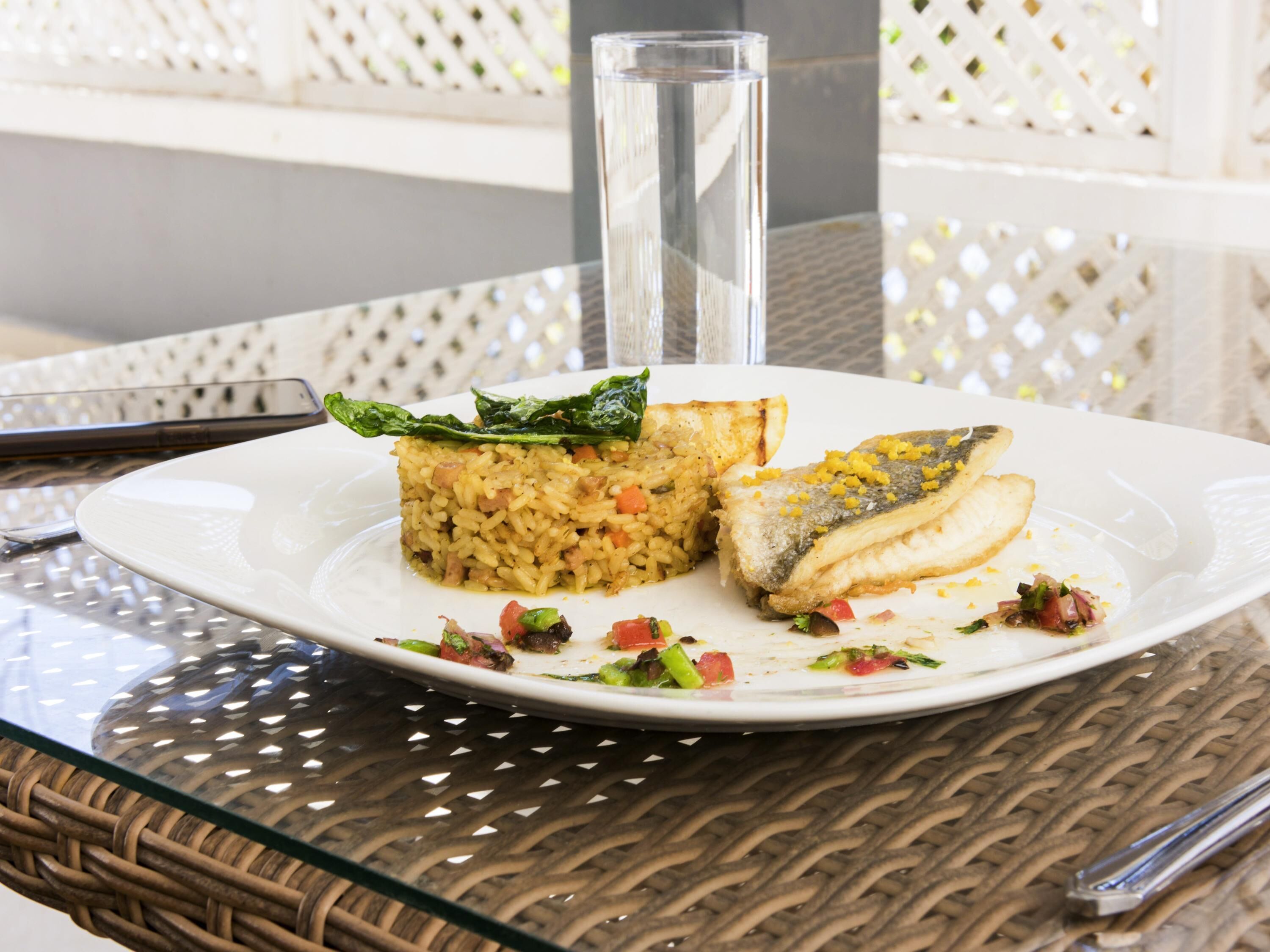 Un plato de comida sobre una mesa de vidrio, con una silla de mimbre al fondo.