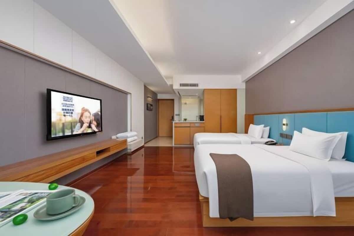 Une chambre d’hôtel équipée d’une télévision, de deux lits, d’un coin repas avec une table et des chaises, et d’une kitchenette.