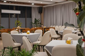 Uma sala de conferências com mesas redondas, cadeiras e uma tela grande.