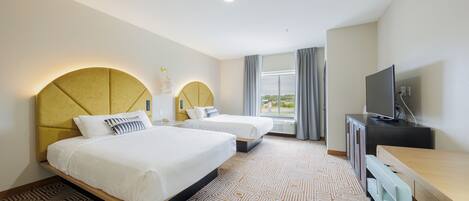 A hotel room with two beds, a desk, a television, and a large window with curtains.