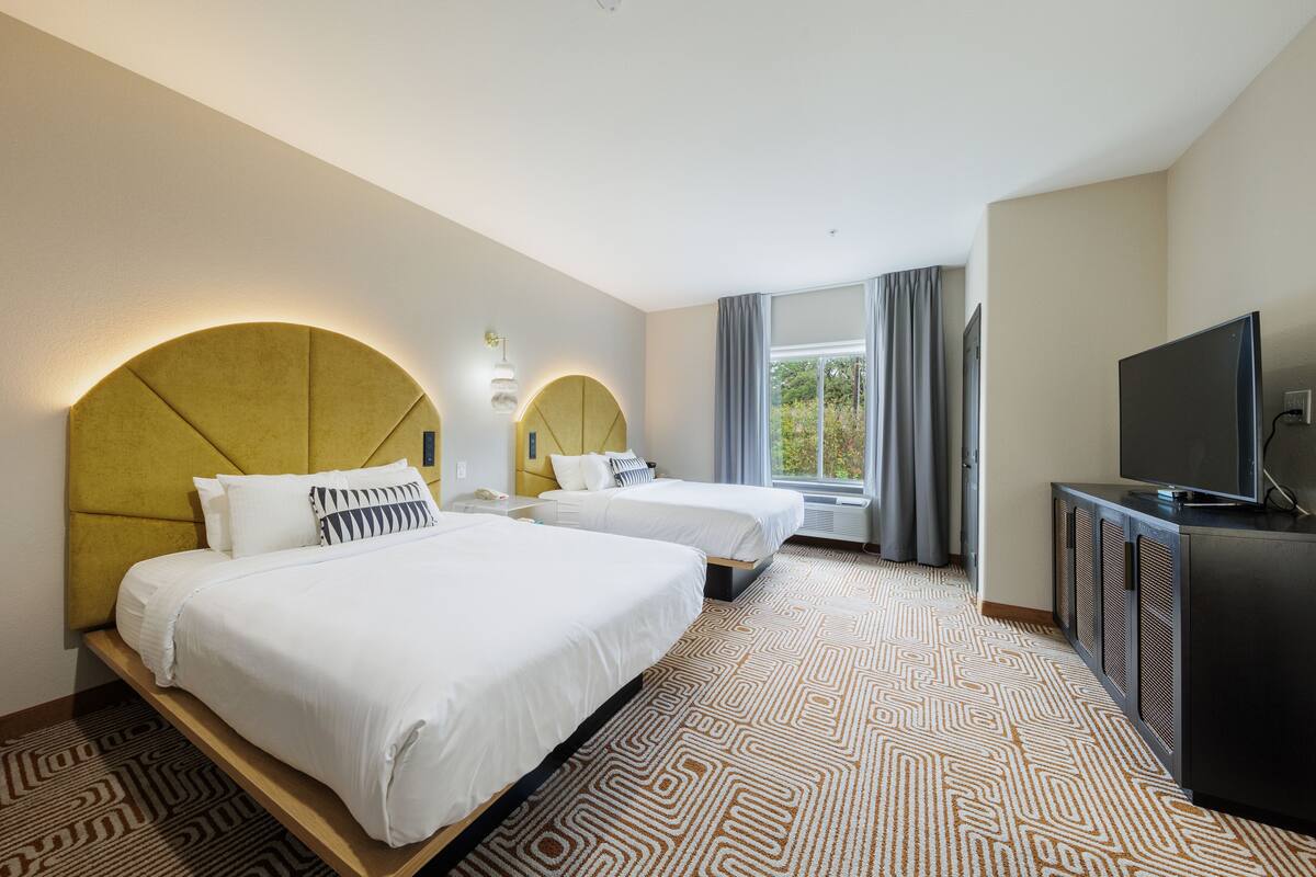 A hotel room with two beds, a television, and a large window with curtains.