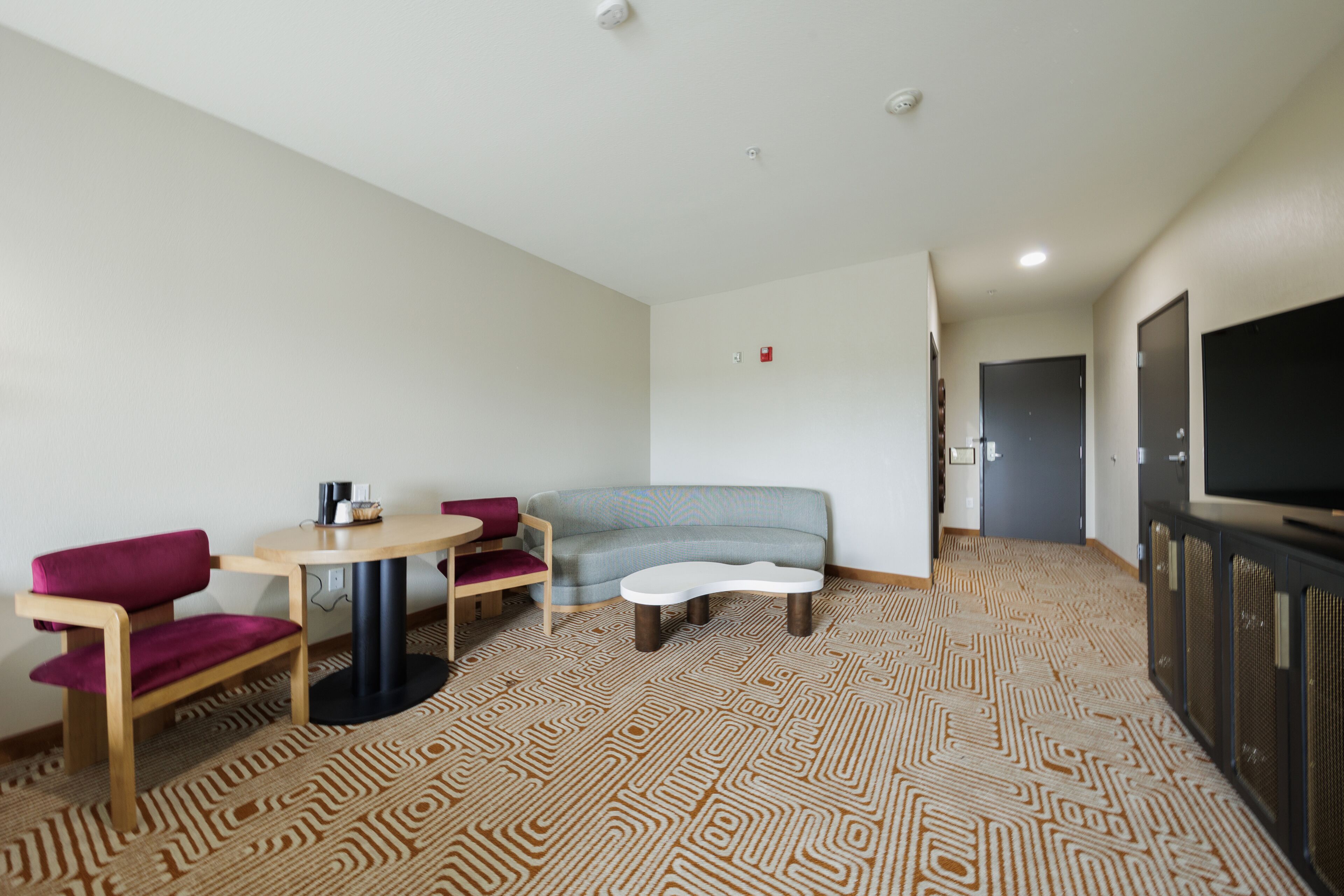 Een moderne hotelkamer met een bank, een tafeltje, een televisie en een kamerbreed tapijt met dessin.