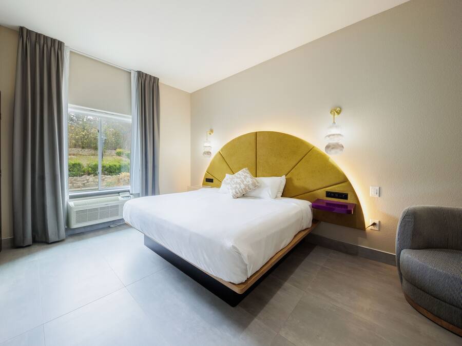 Une chambre d’hôtel moderne dotée d’un grand lit, d’un canapé, d’une fenêtre avec des rideaux et d’un radiateur intégré.