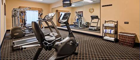 Quarto de hotel com área de ginásio, incluindo esteira, elíptica e aparelhos de musculação.