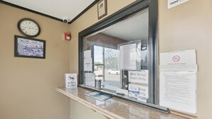 A reception desk with a clock, framed picture, and various informational signs including a no pets policy and a mini shop cash only sign.