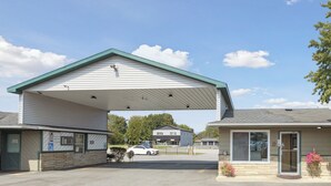 A motel with a covered parking area, a visible entrance, and a small parking lot.