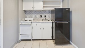 A compact kitchen with white cabinets, a stainless steel refrigerator, a stove, and a tiled backsplash.