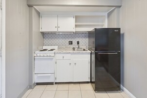 Una cocina compacta con alacenas blancas, un refrigerador de acero inoxidable, una estufa y un salpicadero de azulejos.
