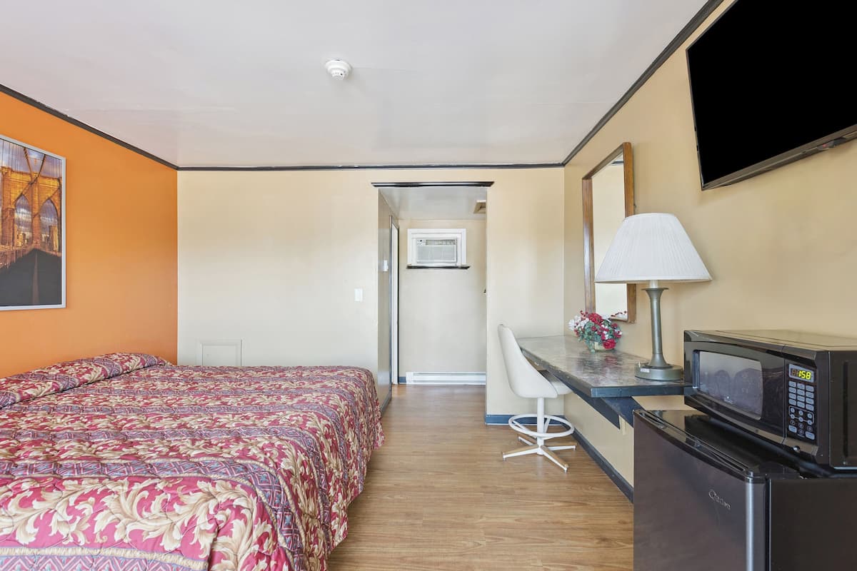 A hotel room with a bed, a desk, a microwave, and a refrigerator.