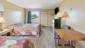 A hotel room with two beds, a desk, a dining table, a TV, and a window with curtains.
