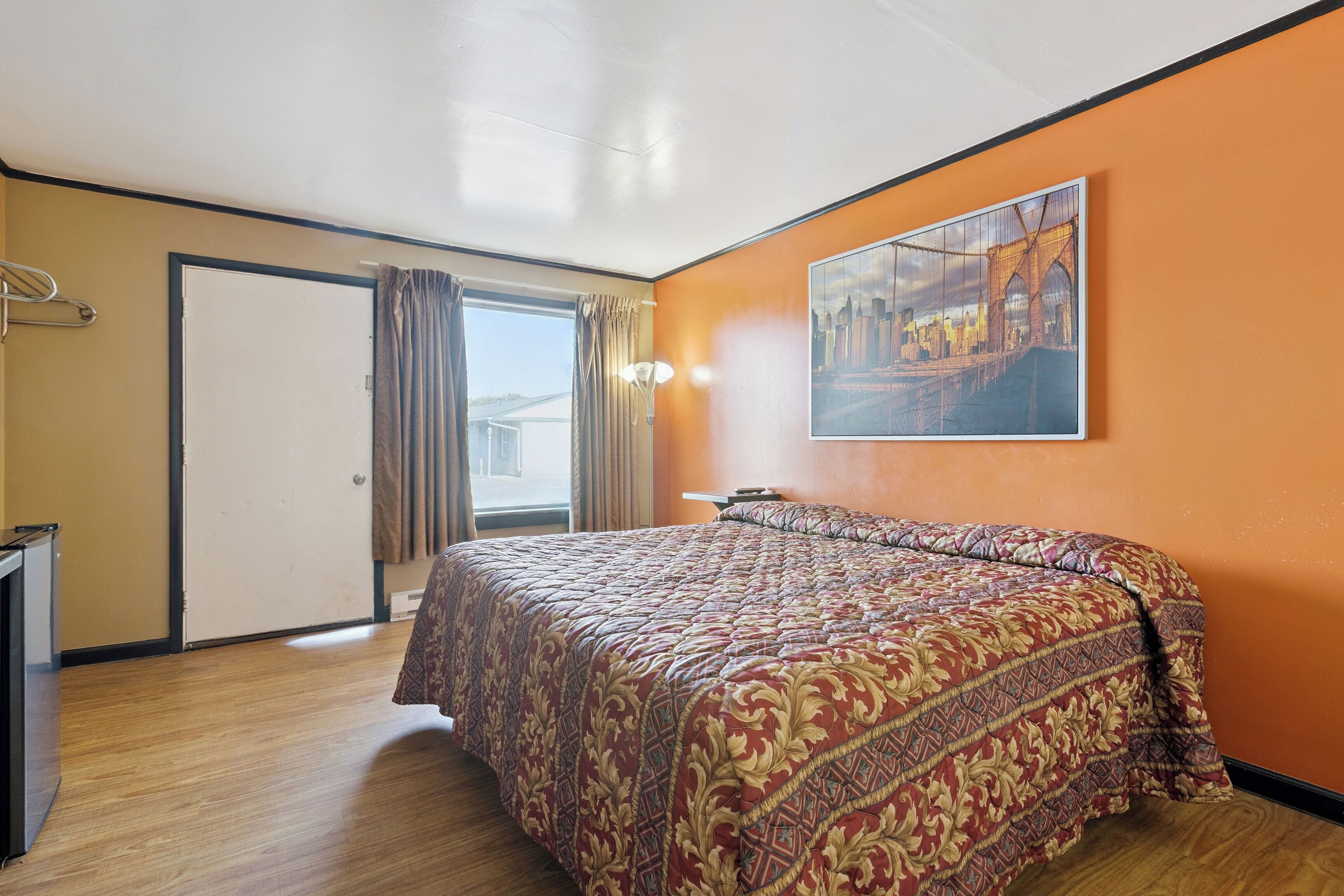 A hotel room with a large bed, a painting on the wall, a door, and a window with curtains.