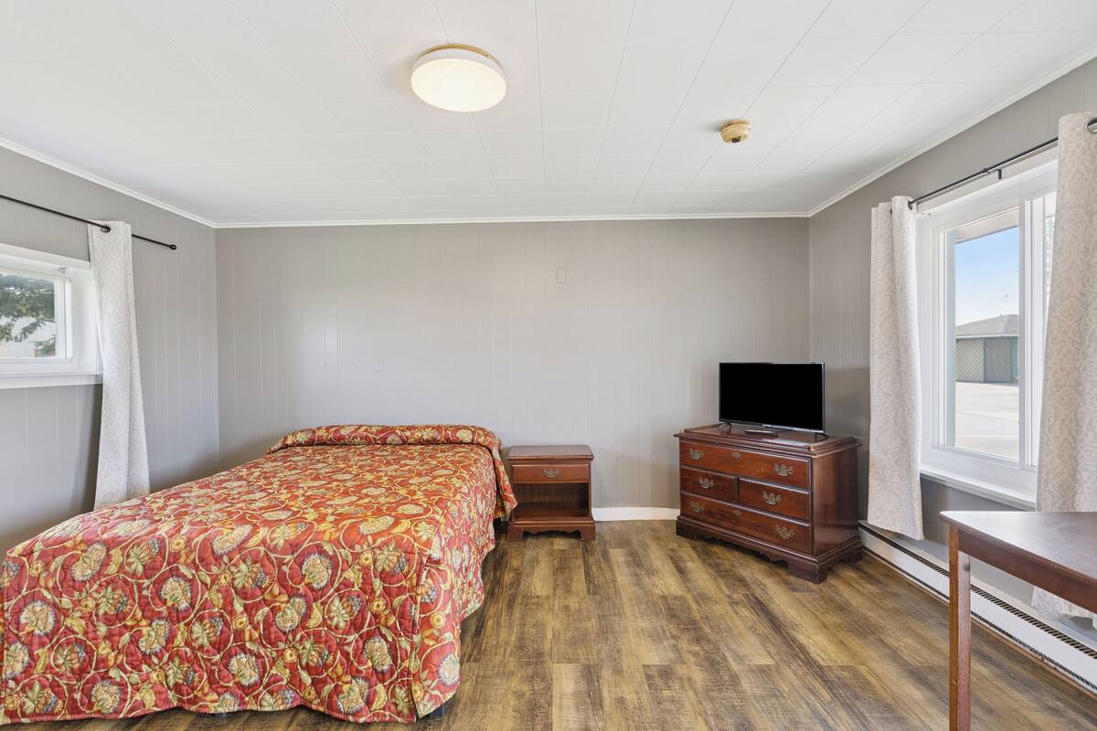 A bedroom with a bed, a dresser, a television, and a window.
