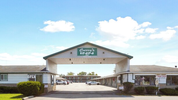 A Curry's Inn motel with a covered parking area, a visible barber shop, and a clear sky. - Curry’s Motel by OYO Saginaw MI (Saginaw)