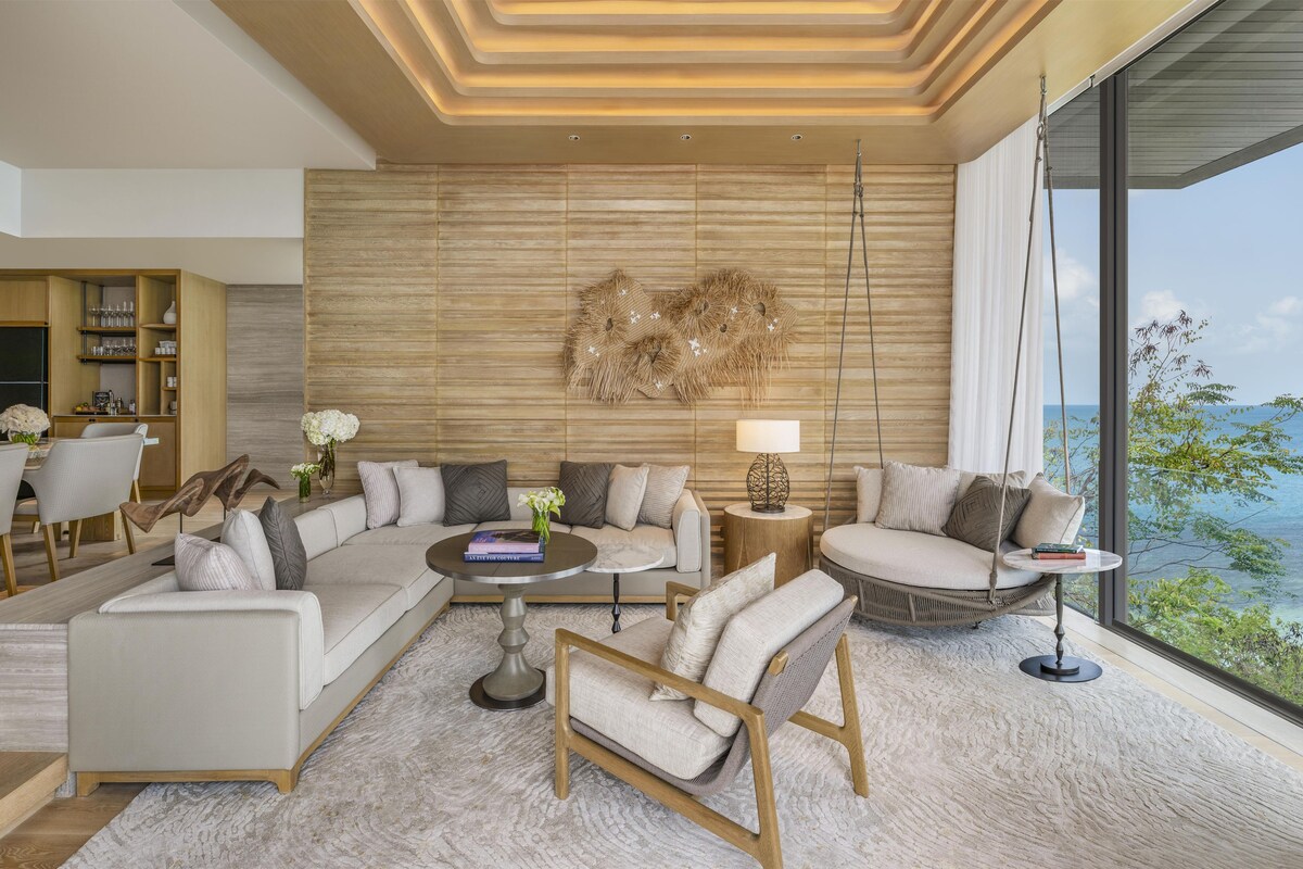 A modern living room with a sofa, armchairs, a coffee table, and a dining area with a wooden cabinet and chairs.