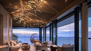 A modern interior with a sofa, wicker chairs, and a view of the sea.