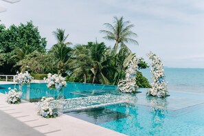 A poolside area with clear water, surrounded by lush greenery and palm trees.