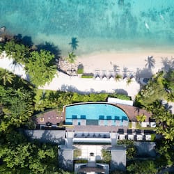 Relax by the inviting pool surrounded by lush greenery and palm trees, with access to a sandy beach and sun loungers.