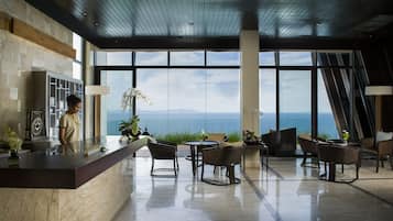 Un moderno vestíbulo de hotel con una recepción, zona de estar y grandes ventanales con vistas al océano.