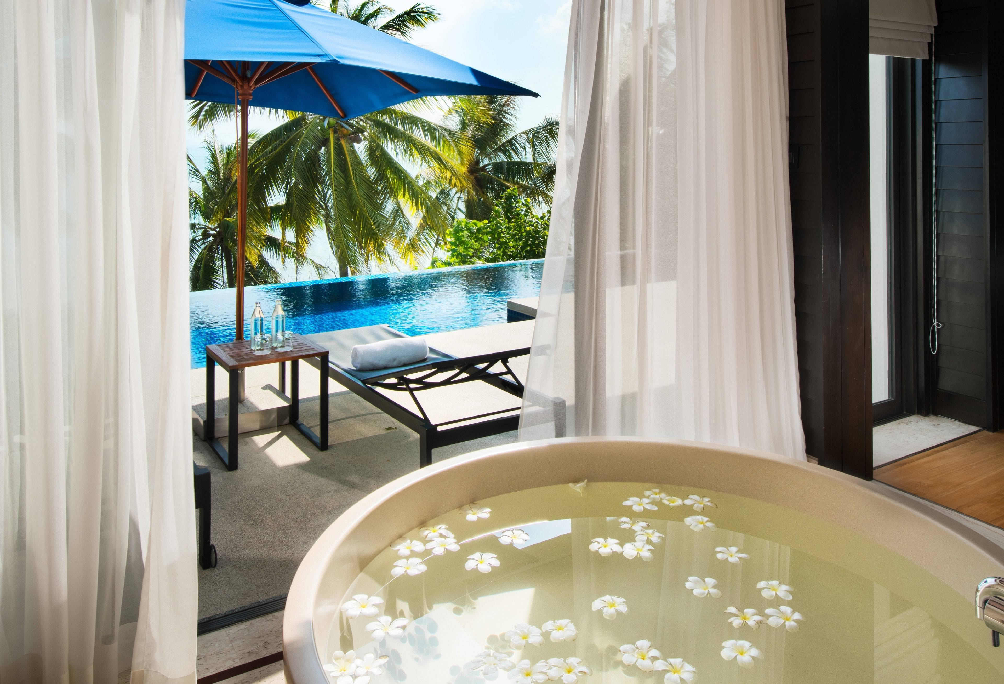 Un balcon privé avec une piscine, une chaise longue et une table agrémentée d’un parasol bleu.